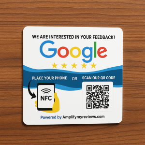 A square feedback sign on a wooden surface displaying the Google logo with five gold stars underneath. The text reads “We are interested in your feedback!” and “Place your phone or scan our QR code.” On the left is an illustration of a hand holding a phone with an NFC symbol, and on the right is a QR code. The bottom text says “Powered by Amplifymyreviews.com.”